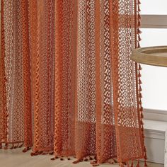 an orange lace curtain with tassels hanging from it's sides in front of a window