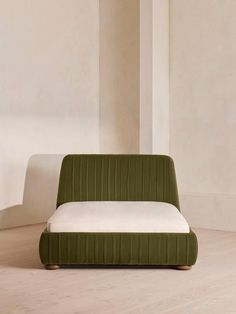 a green couch sitting on top of a hard wood floor next to a white wall