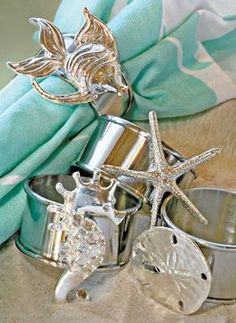 three silver rings with seashells and starfish on them sitting in the sand