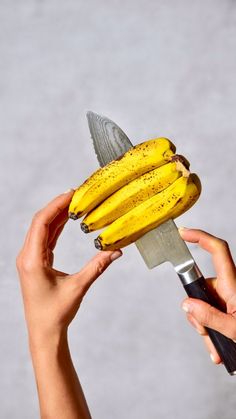 a person holding a knife with some bananas on top of it in front of them