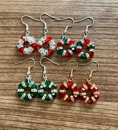 four pairs of christmas themed earrings on a wooden surface with beads and bows hanging from them