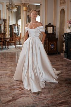 a woman in a white wedding dress standing on the floor with her hands behind her back