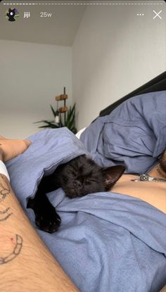 a man laying in bed with his arm wrapped around a black cat sleeping on top of him