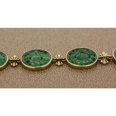 An expertly crafted estate bracelet featuring nine dark green carved nephrite bezel set in 18K yellow gold. The links are attached using ornamental gold bows. The secure discreet lock also serves as a part of the design.  Bracelet Length: 8.00 inches  Bracelet Width: 0.55 inches Luxury Carved Jewelry For Formal Occasions, Formal Yellow Gold Intaglio Bracelets, Formal Yellow Gold Intaglio Bracelet, Yellow Gold Intaglio Bracelet For Formal Occasions, Luxury Green Engraved Jewelry, Luxury Carved Bracelet Jewelry, Luxury Engraved Green Jewelry, Elegant Green Cabochon Bracelets, Luxury Intaglio Bracelets For Gifts