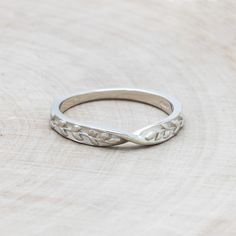 a silver ring sitting on top of a piece of wood with an intricate design in the middle