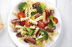 pasta salad with sausage, broccoli and tomatoes on a white plate next to crackers