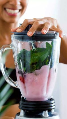 a woman smiles as she uses a blender filled with ingredients to make a smoothie