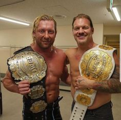 two men standing next to each other holding wrestling belts