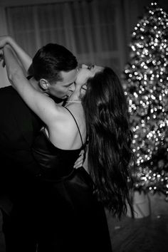 black and white photo of a couple dancing in front of a christmas tree with lights