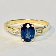 a gold ring with an oval blue stone and baguettes on the side, sitting on a white surface