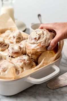 a person dipping some kind of food into a casserole dish with cinnamon rolls