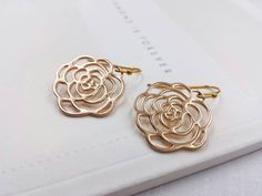 These are pair of beautiful camellia rose earrings. They are made with golden plated over brass flower shaped filigree pendants. The flower is available in two different golden color. The gold color is in a deep gold; and light gold color is in a light gold tone. The earrings measure about 31mm (1.25 inches) from the top of the ear wires to the bottom of the flower. They are perfect for many occasions, gift giving or as a little treat for yourself. Your earrings will presented in a jewelry gift Gold Flower Earrings For Bridesmaid Gift, Gold Rose Design Earrings For Anniversary, Nickel-free Gold Flower Earrings For Wedding, Gold Earrings With Rose Design For Gift, Gold Earrings With Rose Design As Gift, Elegant Gold Flower Earrings Nickel Free, Rose Gold Flower Earrings For Formal Occasions, Gold Flower Earrings For Bridesmaids, Rose Gold Earrings With Rose Flower Design