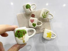 someone is holding some miniature tea cups with trees on them and hearts painted on them