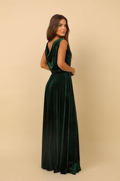 a woman wearing a green velvet dress with open back and side slits, standing in front of a beige background