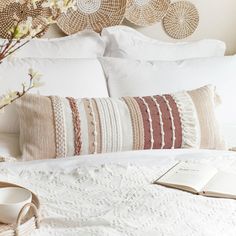 a white bed topped with pillows and blankets next to a vase filled with flowers on top of a wooden headboard