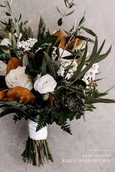 a bridal bouquet with white and brown flowers on the side, in front of a gray wall