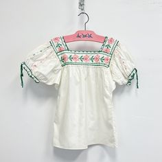 Vintage Childs embroidered peasant top featuring; a square neckline both front and back short pouffy sleees with  a drawsting at the cuff cut straight across the bottom the neckline is embroidered with cross stitched flowers Of a smooth light weight cotton in a crisp white, the embroidery is emerald green, a corally pink, and a darker pink. With no labels or tags, measurements when laid out flat are; 15 inches pit to pit 6 inch sleeve 16 1/4 inches across the bottom 19 1/4 inches from shoulder t Embroidered Peasant Top, Vintage Smocked Bodice Top For Summer, Spring Cotton Peasant Top With Square Neck, Vintage Summer Tops With Smocked Bodice, Cotton Peasant Top With Smocked Bodice And Puff Sleeves, Spring Bohemian Blouse With Square Neck, Spring Bohemian Square Neck Blouse, Bohemian Square Neck Blouse For Spring, Casual Floral Embroidery Square Neck Top