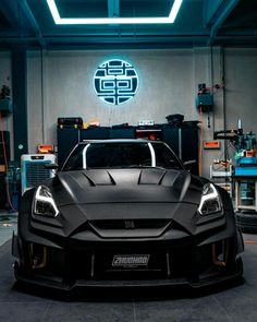 the front end of a black sports car in a garage with blue lights and equipment