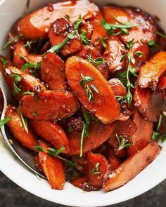 a white bowl filled with cooked carrots covered in sauce and garnished with fresh herbs