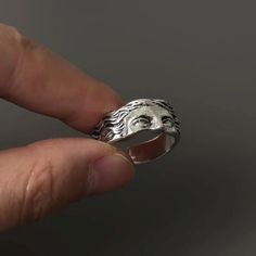 a person is holding a silver ring with a face on it