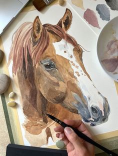 a person is painting a horse with watercolors on paper and using a brush