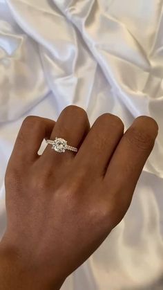 a woman's hand with a diamond ring on top of her left hand and white fabric in the background