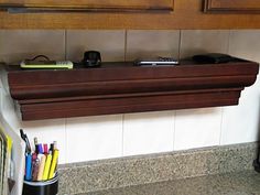 a wooden shelf with pens, pencils, and cell phone on it in a kitchen