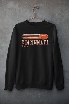 a black sweatshirt with the words cincinnati on it hanging from a hanger against a concrete wall