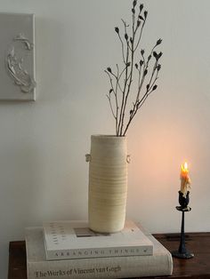 a vase sitting on top of a wooden table next to a book and lit candle