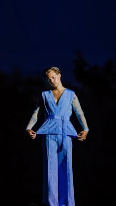 a woman in a blue jumpsuit standing on a stage with her hands on her hips