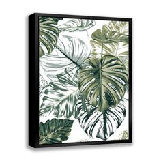 a green and white tropical leaf print on a black framed canvas wall mounted in an empty room