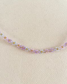 the beaded necklace is laying on top of the white sheeted surface, with tiny flowers all over it