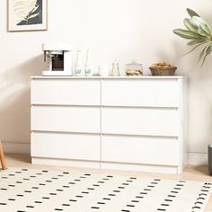 a white dresser sitting in a living room next to a potted plant on top of a rug