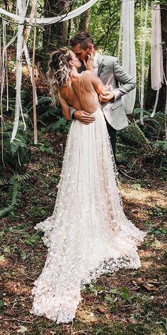 a bride and groom kissing in the woods with streamers hanging from the trees behind them