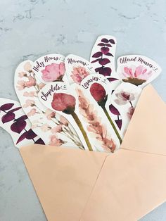 an envelope with some flowers in it on top of a marble table and the envelope is open