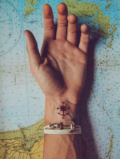 a person's hand with a small anchor tattoo on it, sitting in front of a map