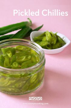 pickled chilies in a glass jar with spoons on the side and pink background