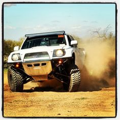 a white truck driving down a dirt road with dust coming from the front tire tracks