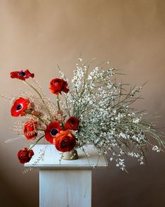 a vase filled with red and white flowers on top of a wooden table next to a wall