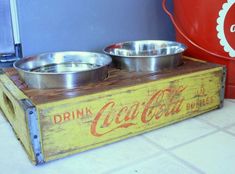 two metal bowls sitting on top of a wooden crate next to a coca cola can