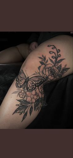 a woman's thigh with flowers and a butterfly tattoo on her leg, while she is laying down