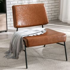 a brown leather chair with a blanket on it's back in front of a brick wall