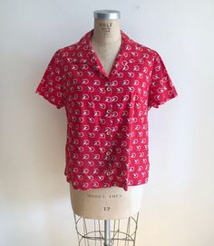 "Short-sleeved, red, white, and blue flag print shirt, from the 1940s. Bust measures 22.5\" (57 cm) flat across and waist measures 22\" (56 cm) flat across. The blouse is 26\" (66 cm) in length. Cotton." Vintage Red Camp Shirt With Camp Collar, Retro Red Short Sleeve Camp Shirt, Red Retro Shirt With Camp Collar, Retro Red Shirt With Camp Collar, Vintage Red Short Sleeve Camp Shirt, Retro Red Cotton Camp Shirt, Casual Red Shirt With Retro Print, Red Vintage Print Cotton Top, Red Cotton Tops With Vintage Print