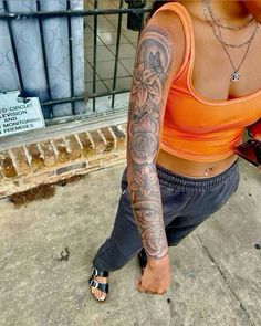 a woman sitting on the ground with tattoos on her arm