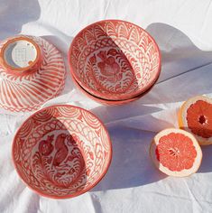 three oranges sitting on top of a table next to two bowls and one cut in half