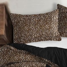 a bed with leopard print sheets and pillows on top of it next to a wooden headboard