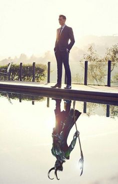 a man in a suit standing on the edge of a pool with his hands on his hips