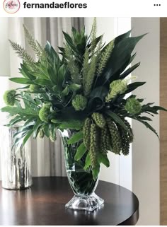 a vase filled with green plants on top of a wooden table