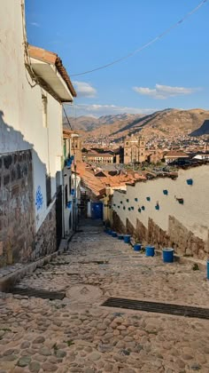 a cobblestone street with blue buckets on the side and buildings in the background