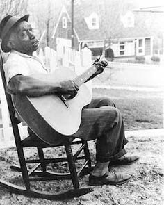 a black and white photo of a man sitting in a chair playing an acoustic guitar